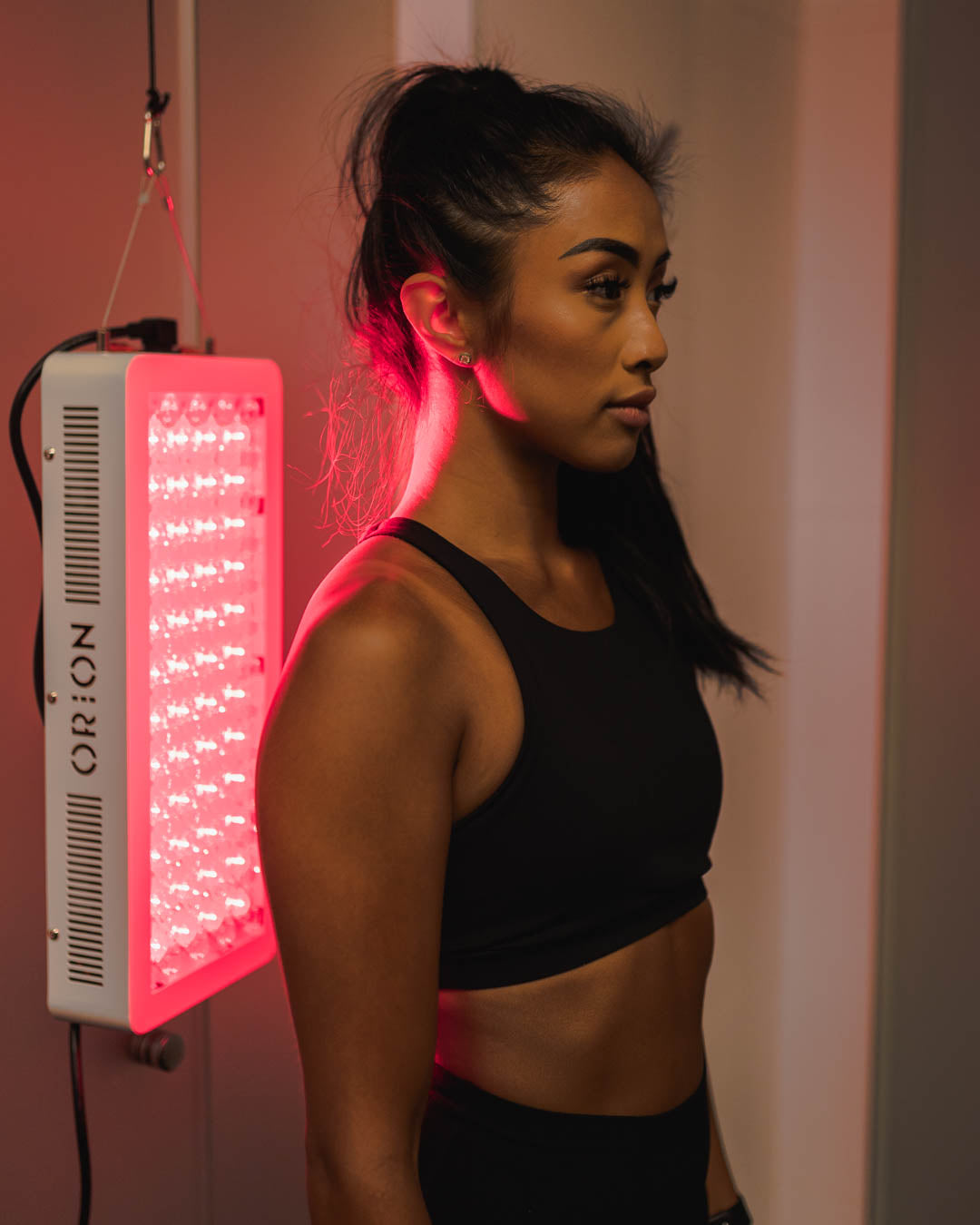 Woman facing away from the Orion 500 to receive direct treatment to the back side of her body. Orion Red Light Therapy.