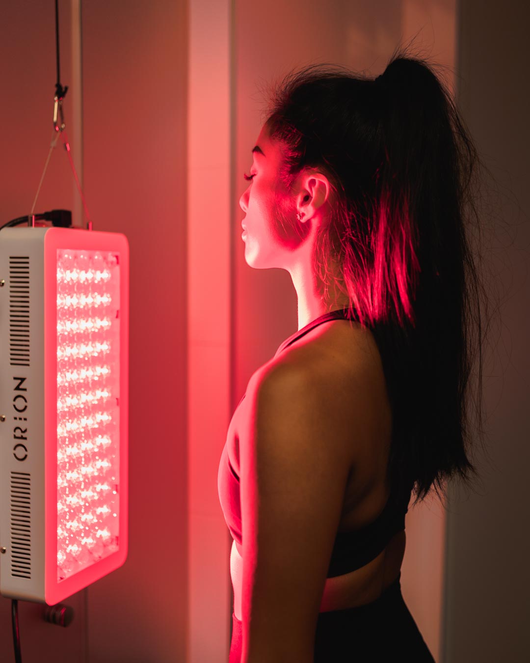 Woman facing towards the Orion 500 for directed treatment towards the front side of her body. Orion Red Light Therapy.